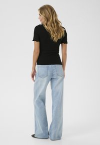 Haut noir à côtes avec de courtes manches volantées, associé à un pantalon en jean large bleu clair avec des poches arrière et une finition délavée.