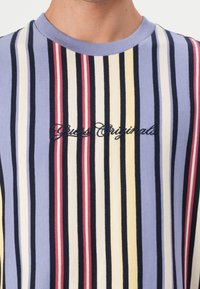 Striped t-shirt in soft cotton fabric, featuring vertical lines in blue, white, yellow, and red. "Guess Originals" logo embroidered in black.