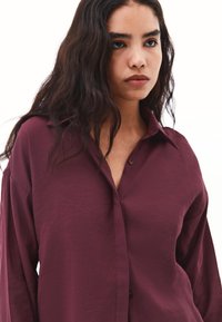 Camicia bordeaux con bottone, colletto a risvolto, vestibilità rilassata e maniche lunghe, realizzata in un tessuto testurizzato.