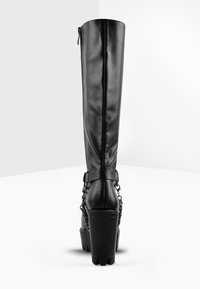 Knee-high black faux leather boots with a chunky heel, side zipper, and chain detail around the ankle. Smooth texture and sleek design.