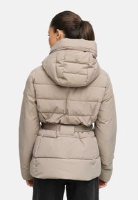 Beige pufferjacka med åtsittande midja, släta sömmar och huva. Designen har en diskret logotypdetalj på baksidan. Slät textur.