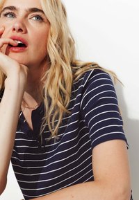 Polo shirt bleu marine à manches courtes avec des rayures blanches horizontales, présentant un col à bouton et un tissu texturé. Coupe décontractée et ample.