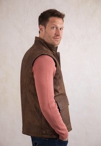 Brown leather vest with quilted design, zip closure, and snap pocket detail, worn over a pink ribbed long-sleeve shirt.