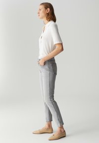 Jean gris clair avec une coupe slim, poches avant et détail à zip à la cheville, associé à une chemise blanche à manches courtes et des ballerines beiges.