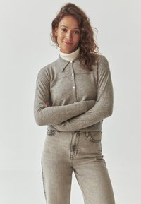 Graues Langarm-Polohemd mit Knopfleiste und weißem Kragen, kombiniert mit hellgrauen hochtaillierten Jeans. Strukturiertes Strickmaterial.