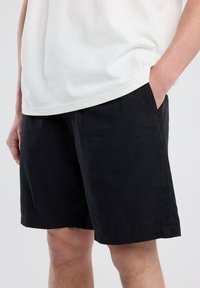 Black cotton shorts with side pockets, relaxed fit, and a simple design. Hem finishes are clean without visible embellishments.