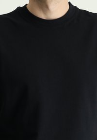 Camiseta negra de cuello redondo, hecha de algodón suave, con un diseño simple sin patrones ni acentos. Ajuste clásico y color sólido.