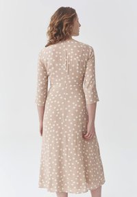 Beiges Midi-Kleid mit weißen Polka-Punkten, dreiviertelÄrmeln und gerader Silhouette. Der Rücken hat eine Mittelnaht und dezente Details.