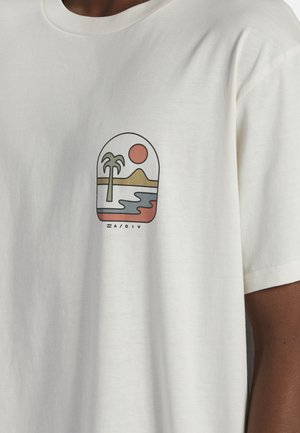 T-shirt blanc avec un petit dessin représentant un palmier, le soleil, des montagnes et de l'eau en couleurs atténuées sur le côté gauche de la poitrine.