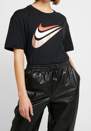 Black cotton t-shirt featuring a large Nike logo in red, white, and metallic rose gold; paired with black faux leather pants with elastic waist.