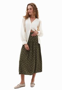 Crème button-down blouse met pofmouwen, gecombineerd met een groene rok met stippen. Sandkleurige platte schoenen maken de outfit af.