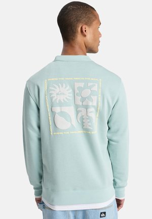 Sweat-shirt bleu clair à manches longues, poignets côtelés, avec des motifs graphiques blancs au dos et un logo sur l'ourlet inférieur.