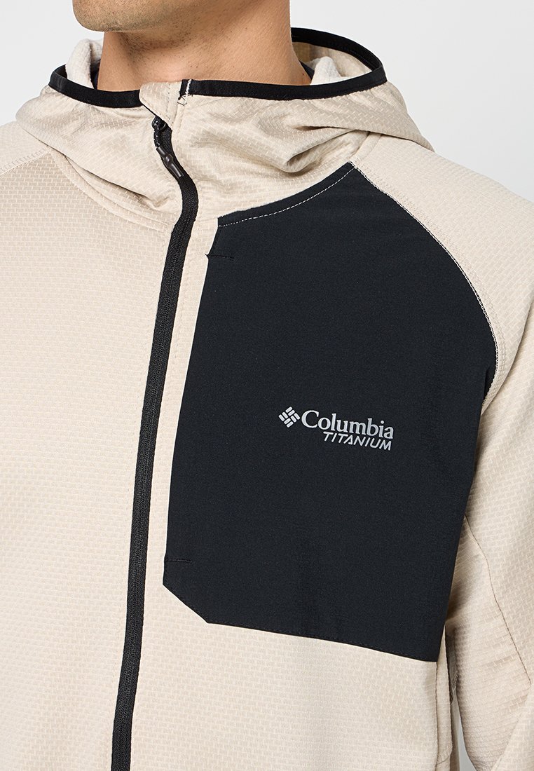 Jasnoszara, pikowana kurtka z kapturem z fakturowanym wzorem, czarną kieszenią akcentową i logo Columbia Titanium. Wykonana z materiału syntetycznego.