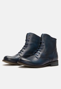 Botas de cuero azul oscuro hasta el tobillo con una textura suave, diseño de cordones y un tacón bajo. Presenta un logo sutil en el costado.