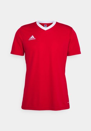 Czerwona sportowa koszulka Adidas z krótkim rękawem, białym kołnierzem w kształcie litery V i logo Adidas na prawej piersi na neutralnym tle.