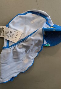 Blue sun hat with a scalloped edge and light blue interior featuring small colorful patterns. Tag attached with care instructions.