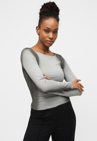 Γκρι μπλούζα μακρυμάνικη με εφαρμοστή σχεδίαση, στρογγυλή λαιμόκοψη, ραβδωτή υφή και αντίθετα πιο σκούρα μανίκια. Συνδυάζεται με μαύρο παντελόνι.