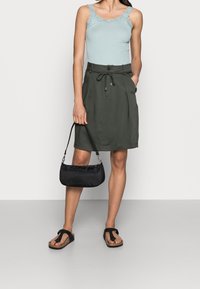 Ljusa blå ribbade linne med spetskant, olivgrön kjol med dragsko, svart mini-väska och svarta flip-flops med tårstöd.