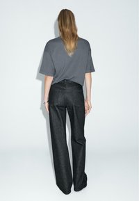 T-shirt grigio oversize abbinato a pantaloni larghi neri in denim a vita alta. Il tessuto appare liscio, con semplici dettagli di cucitura.