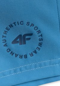 Tissu bleu avec logo noir "4F" et texte circulaire "Authentic Sportswear Brand", avec des détails de couture visibles.