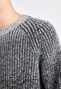 Maglione lavorato a maglia con un motivo a righe grigie e nere, colletto a coste e tessuto texturizzato. Primo piano della spalla e del colletto.