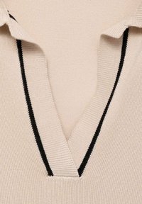 Beige Strickpolo mit V-Ausschnitt, versehen mit einem schwarzen Akzentstreifen entlang des Kragens. Weicher Texture, taillierte Passform und detaillierte Nähte.