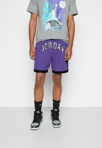 Purple mesh basketball shorts with "JORDAN" in silver lettering. Paired with a grey graphic t-shirt and black socks and sneakers.
