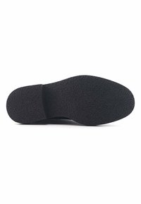 Suela de zapato de goma negra con una superficie texturizada, que presenta una punta curva y un leve tacón. La forma general es redondeada sin marcas visibles.