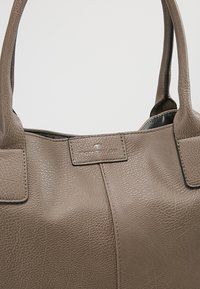 Taupe texturovaná kožená kabelka s dvojitými rukojetmi a jemným raženým logem značky na předním panelu.