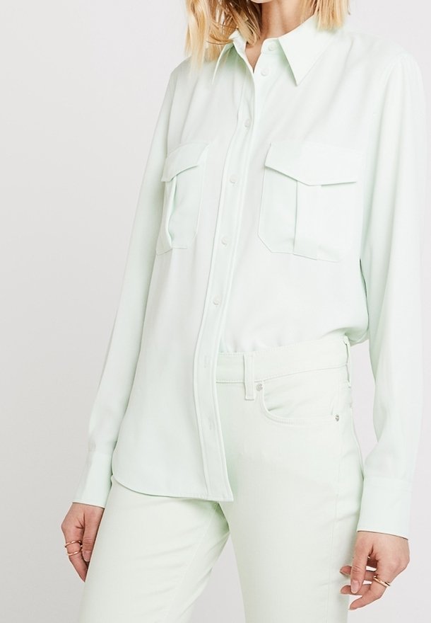 Femme portant une chemise vert clair à boutons avec poches à rabat et un pantalon vert clair assorti, montrée des épaules aux hanches.