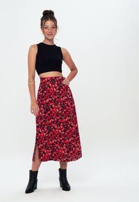 Sort ribbet crop top parret med en rød blomster midi-nederdel med en sideslids. Båret med sorte ankelstøvler. Glat stof med blomsterprint.