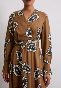 Braunes Wickelkleid mit einem auffälligen Muster in Weiß und Dunkelbraun. Lange Ärmel und eine betonte Taille heben den fließenden Stoff hervor.