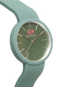 Reloj de silicona verde con esfera redonda, marcadores de hora plateados y un logo rojo. Correa texturizada con pequeñas perforaciones para un mejor agarre.