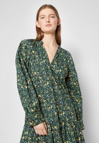 Vestido floral verde com mangas longas, decote em V e saia em camadas. Apresenta pequenas flores amarelas, azuis e brancas sobre um fundo verde escuro.