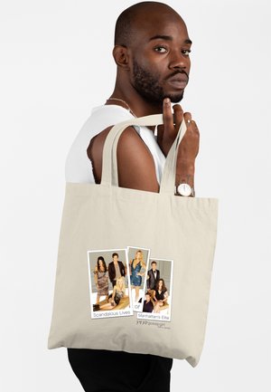 Mann hält eine beige Tragetasche mit einem Besetzungsfoto und dem Text „Skandalöse Leben der Elite von Manhattan“ aus der TV-Serie Gossip Girl.