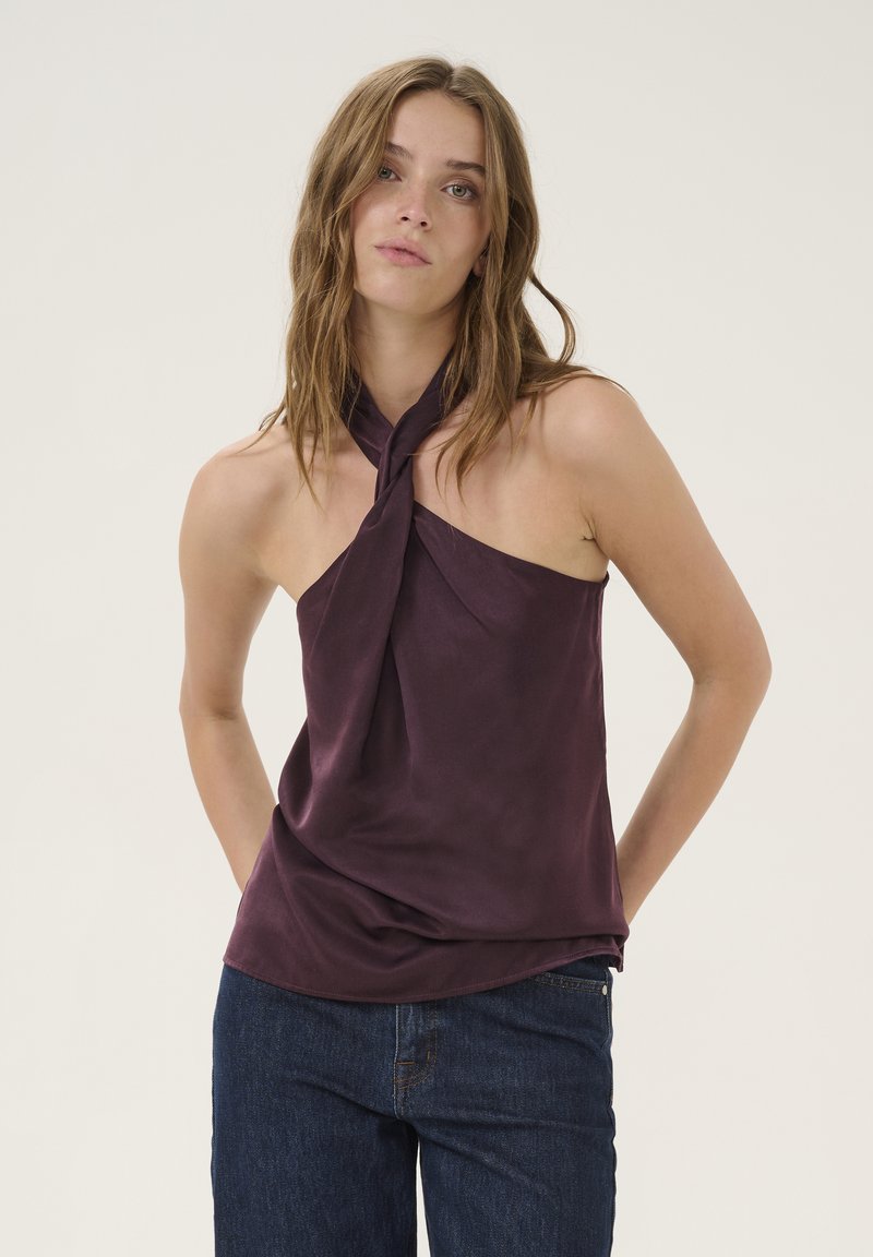 Paarse satijnen haltertop met een knoophals en een vloeiende uitstraling, gecombineerd met blauwe denim jeans. De stof lijkt glad en zacht.