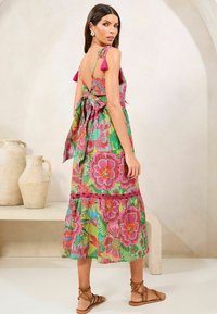 Rochie florală colorată cu un design în straturi, având modele roz și verzi, detaliu cu legare la spate și accente cu ciucuri pe bretele.