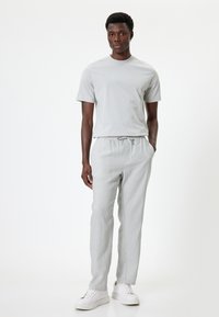 Grijze t-shirt en bijpassende lichte broek, beide met een casual pasvorm. Sneakers in het wit. Gladde textuur, minimalistisch ontwerp, elastische tailleband.