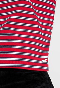 Röd och vit randig t-shirt med marinblå linjer, med en liten vit logotyp vid fållen och mjukt bomullstyg.