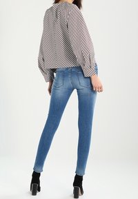 Siniset farkkuhousut, joissa on kapeat lahkeet ja keskitason vyötärö, yhdistetty mustavalkoraidalliseen paitaan. Paidassa on muhkeat hihat ja selän laskos.