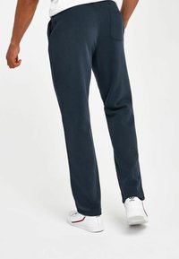 Pantalones de chándal azul marino hechos de una tela suave, con bolsillos laterales, cinturilla elástica y diseño de pierna recta. Combinados con zapatillas blancas.