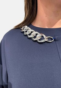 Top blu navy con dettaglio in catena argentata sulla spalla. Il tessuto ha una texture liscia e il design è semplice ed elegante.