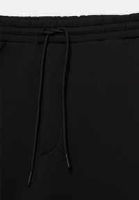 Taille de pantalon de jogging noir avec bande élastique et cordon noir noué en un simple nœud.
