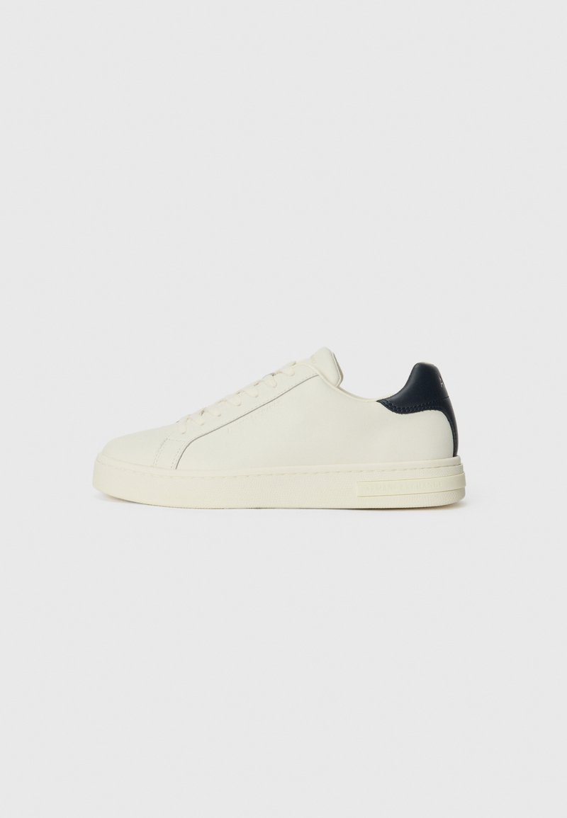 Witte leren sneaker met een marineblauw leren accent op de hak, ronde neus, platte rubberen zool en vetersluiting met zes oogjes.