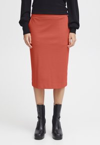 Knie-lange, aansluitende rok in effen roestkleur met een soepele textuur, gecombineerd met zwarte enkellaarzen met een dikke hak.