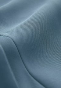 Mehka, teksturirana tkanina v zatemnjeni modri barvi z drobnim rebrastim vzorcem, ki prikazuje nežne valove in gladke konture.