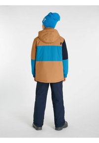 Bunte Winterjacke mit tanfarbenen, türkisfarbenen und marineblauen Abschnitten. Verfügt über eine Kapuze und elastische Bündchen, kombiniert mit dunklen Hosen und schwarzen Stiefeln.