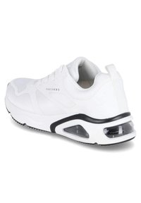Zapatilla deportiva blanca con parte superior de malla, cuello acolchado, acentos negros y unidad de amortiguación de aire en el talón. Presenta un diseño con cordones y suela texturizada.