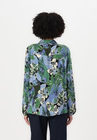 Long-sleeve shirt in a green, blue, and black floral pattern; features a collar and buttons with a loose, relaxed fit.