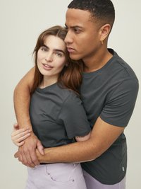 Camisetas ajustadas grises, de mangas cortas, hechas de algodón, llevadas por dos personas en un abrazo. Uno de ellos lleva pantalones de un ligero tono púrpura. Detalles de diseño mínimos.